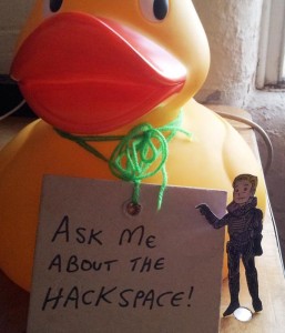 David 8 touches Ein the Duck's sign, which says Ask Me About The Hackspace